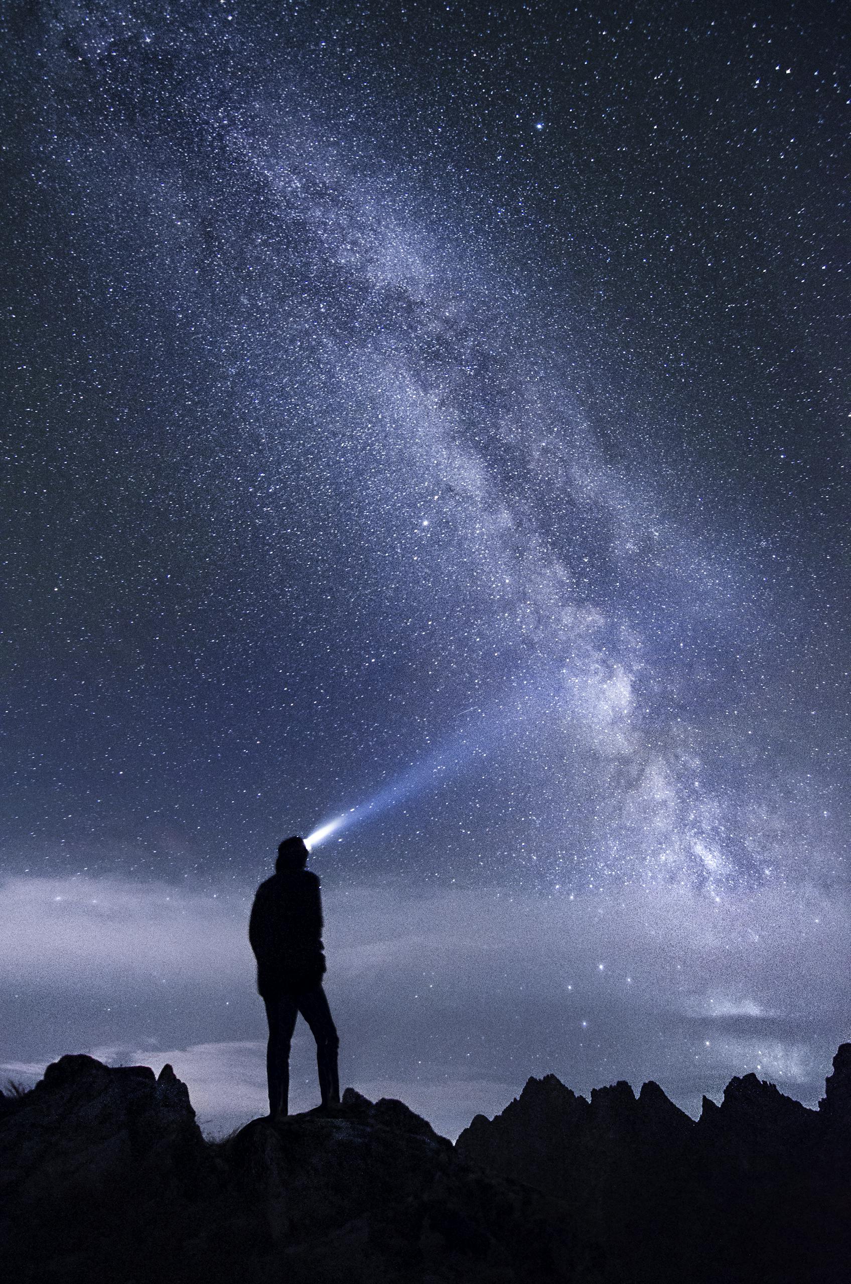 Silhouette of a person exploring the star-studded Milky Way sky at night in the mountains.